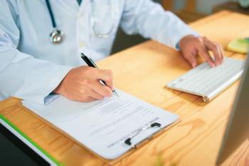 Health care professional writing while using a computer