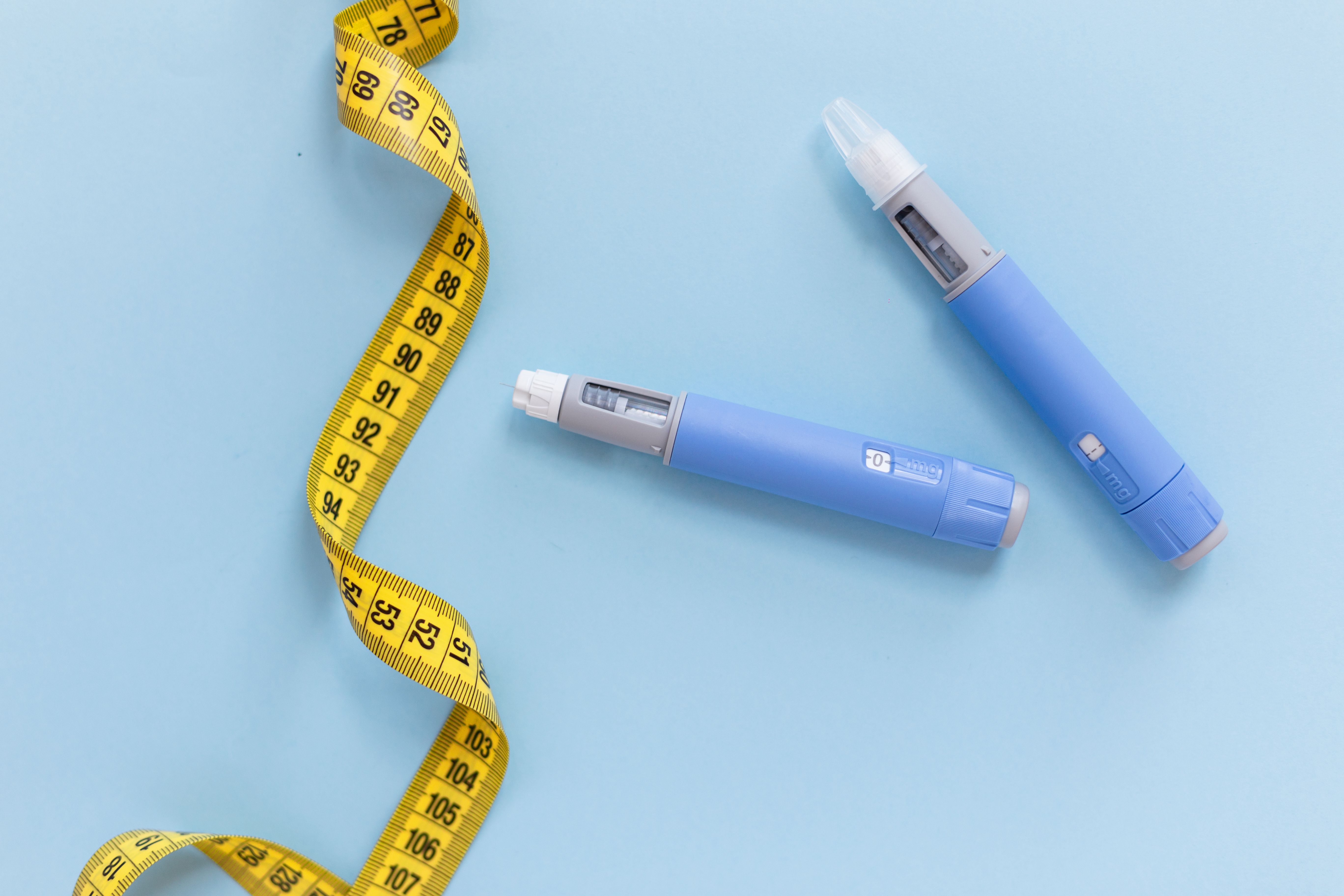 Two drugs injection ozempic for weight loss with a measuring yellow tape on a blue background. Drug pen for diabetics and weight loss, top view. antidiabetic medication or anti-obesity medication - Image credit: alones | stock.adobe.com