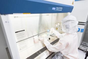 A scientist in sterile coverall gown pipetting medium or reagents for cell culture experiment in biological safety cabinet. Doing biological research in clean environmental.
