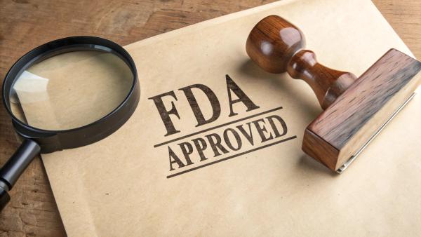 'FDA APPROVED' stamped on textured paper, beside a magnifying glass and wooden rubber stamp, symbolizing certification, quality assurance, and regulatory approval | Image Credit: StocksJust4You | adobe.stock.com