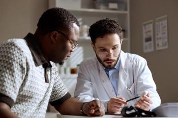 Black middle aged man consulting Caucasian male doctor, reviewing medical device during clinic visit. Useful for healthcare communication, patient trust, diagnosis concepts