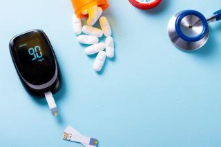White pills in orange bottle with blood glucose meter on blue background