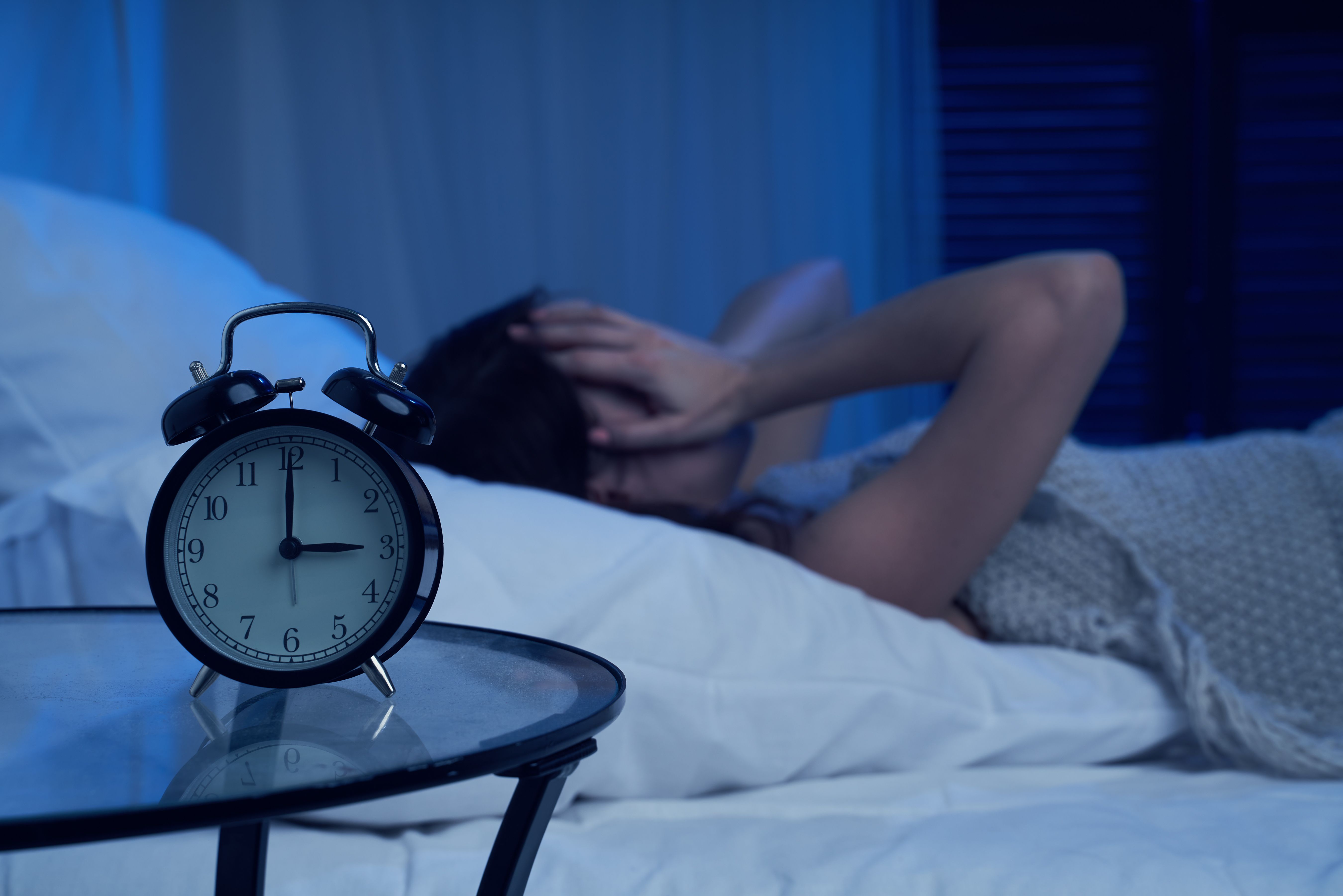 Image credit: Sergey | stock.adobe.com - Unhappy woman with insomnia lying on bed next to alarm clock at night