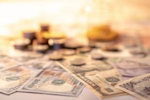 Various of international money coin and banknote with blurred hourglass in the background. Time investment with currency exchange concept. Focus on dollar banknote - Image credit: zephyr_p | stock.adobe.com