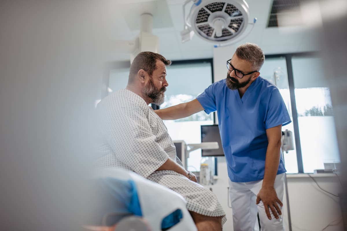 Supportive doctor soothing a worried overweight patient, discussing test result in emergency room. Illnesses and diseases in middle-aged men's health. Compassionate physician supporting stressed 