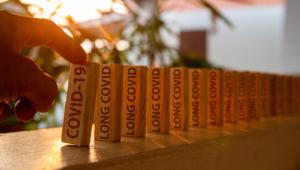 Hand poked on a row of wooden dominoes, with the words "COVID19" on the first piece and the words "LONG COVID" on subsequent pieces - Image credit: Anucha | stock.adobe.com