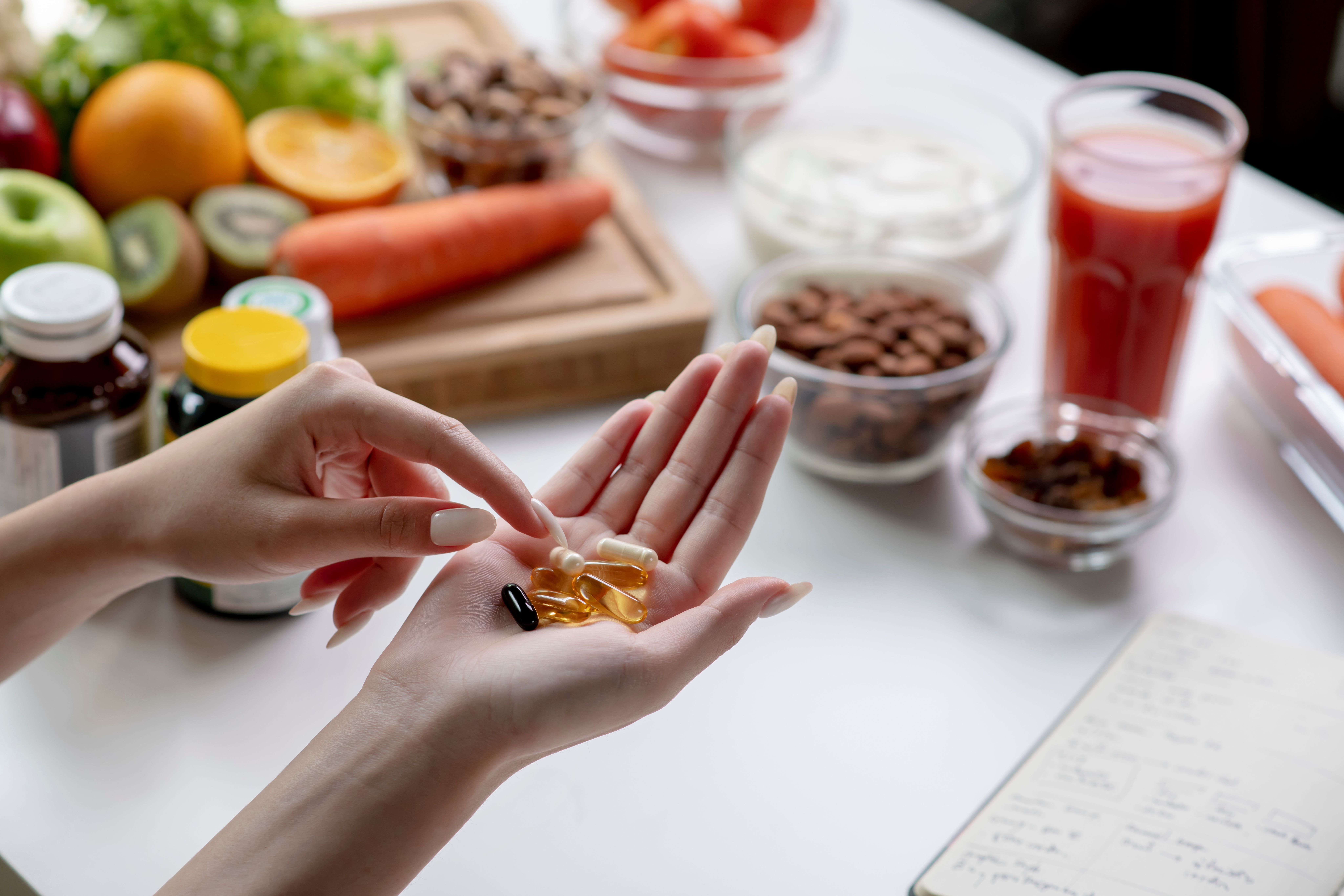 Woman professional nutritionist checking dietary supplements in hand, surrounded by a variety of fruits, nuts, vegetables, and dietary supplements on the table | Image Credit: amenic181 | stock.adobe.com 