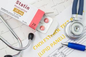Effects and treatment of statins concept photo. Open packaging with drugs tablets, on which is written "Statin Medication", lies near stethoscope, result analysis on cholesterol (lipid panel) and ECG.