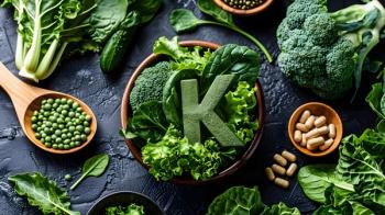Vitamin K Supplements Surrounded by Nutritious Leafy Greens for Optimal Bone Health - Image credit: pkproject | stock.adobe.com 