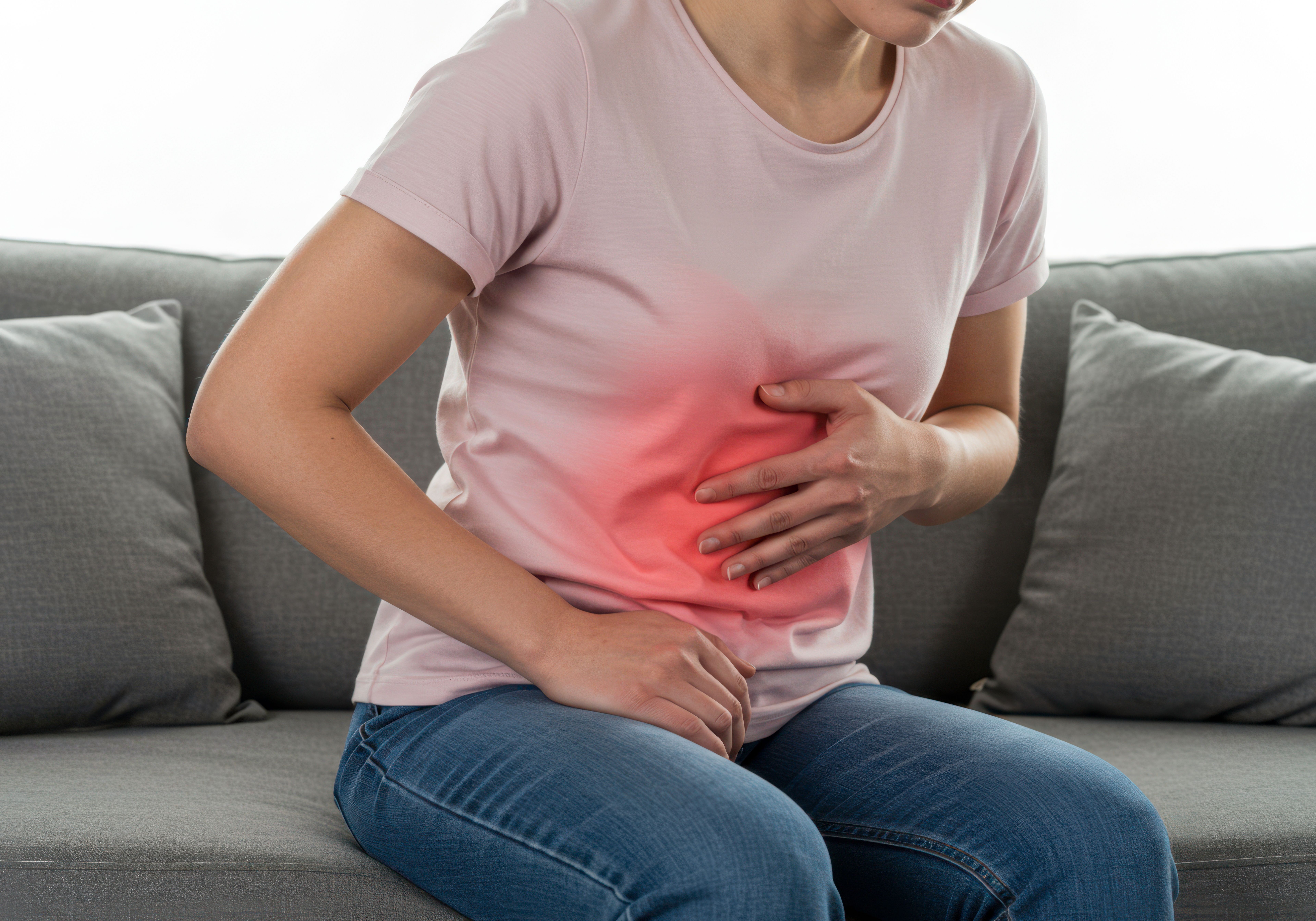 Woman Experiencing Stomach Pain Sitting on a Sofa | Image Credit: J.G Studio | stock.adobe.com
