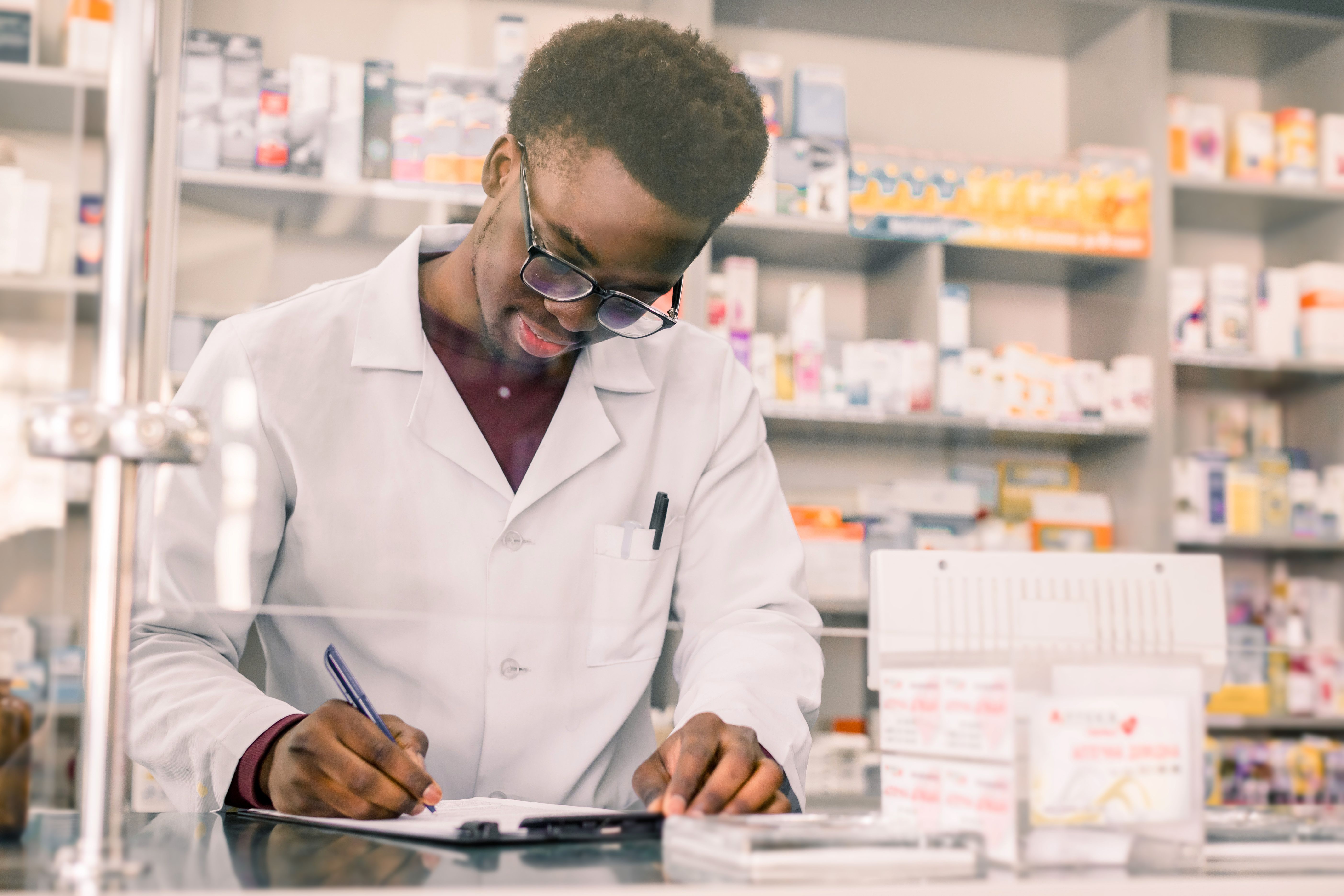 Portrait of a happy African American pharmacist writing prescription at workplace in modern pharmacy - Image credit: sofiko14 | stock.adobe.com