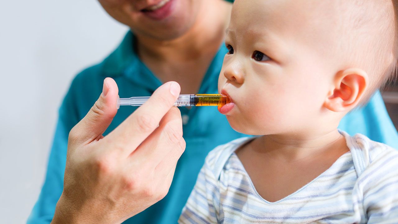 Cute little Asian 1 year old toddler baby boy child feeding with liquid medicine with a syringe, Dad giving remedy to kid who having flu, Fever cold and flu concepts. Selective focus at hand & syringe | Image Credit: ©yAOinLoVE - stock.adobe.com