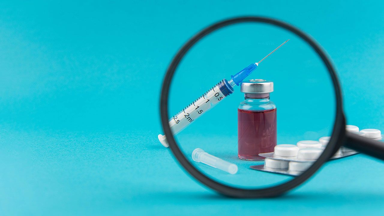 Pharmaceutical research and clinical trials concept. Medicine vial bottle for injection with vaccine and new pharmacy drug in pills and syringe under magnifying glass. Image Credit: © strigana - stock.adobe.com