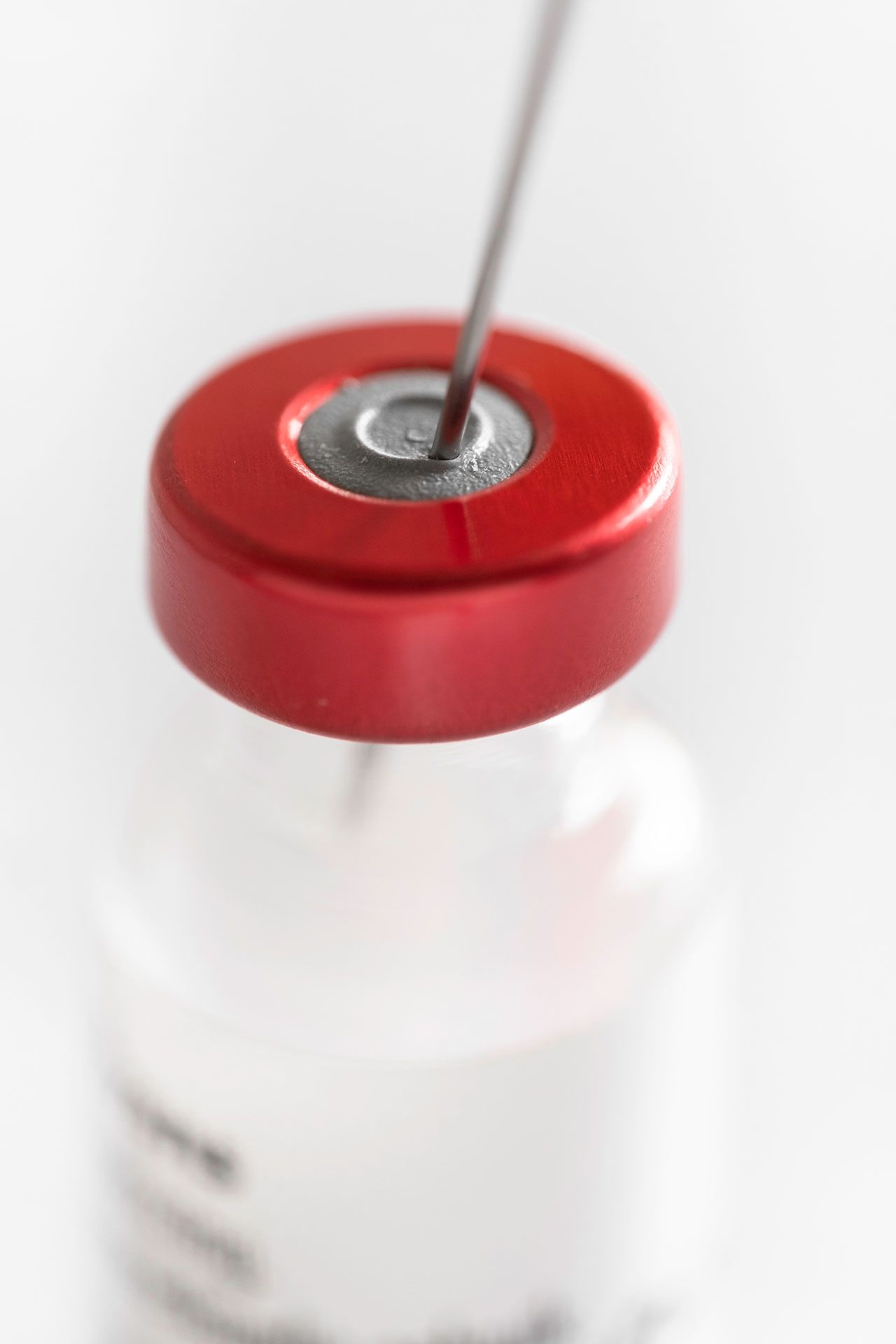 Needle of a syringe protrudes through the rubber cap of a vaccine vial with red cap. Focus on the rubber stopper, shallow depth of field |Image Credit: © Henk Vrieselaar – stock.adobe.com