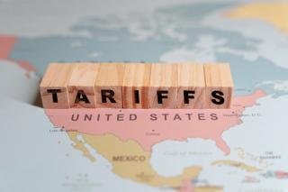 Wooden blocks spelling TARIFFS are placed on a map of North America, specifically over the United States and Mexico | Image Credit: © Rokas - stock.adobe.com