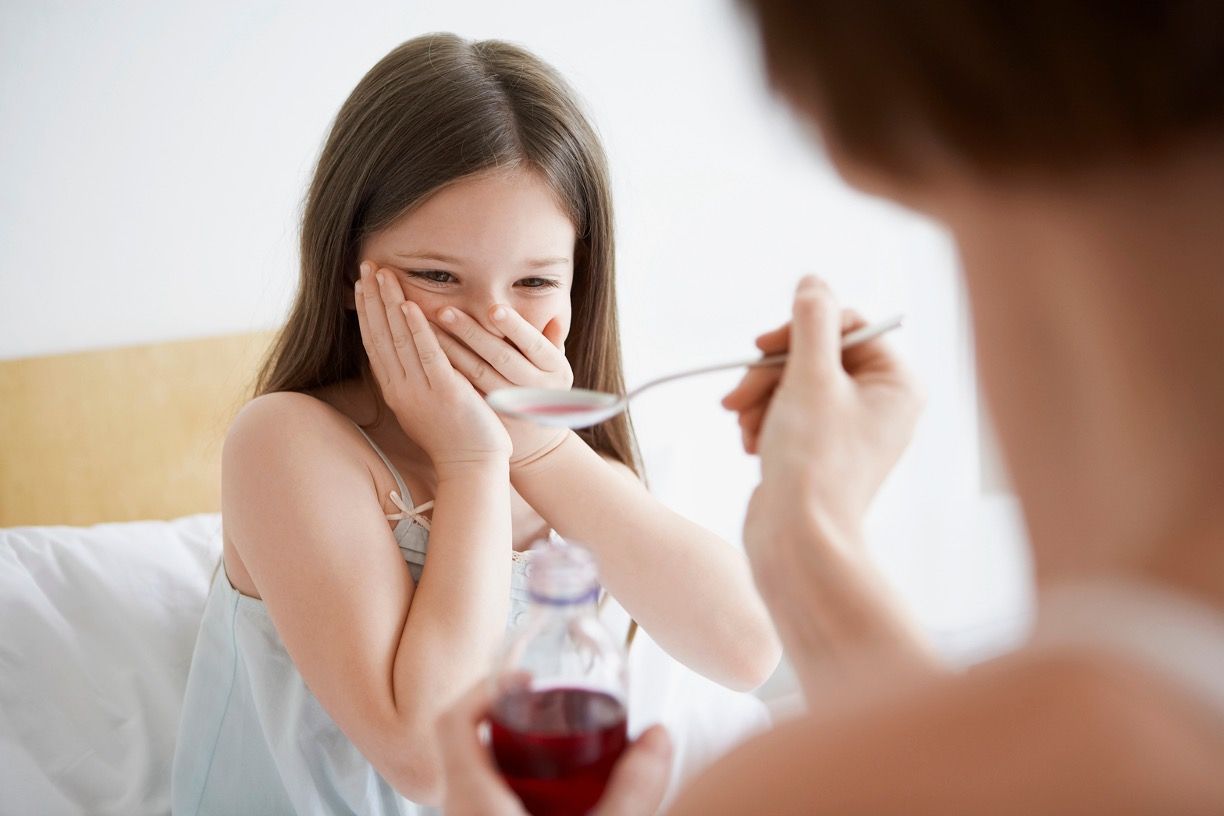 Mother giving over-the-counter (OTC) cough syrup to reluctant daughter in bed © moodboard -chronicles-stock.adobe.com