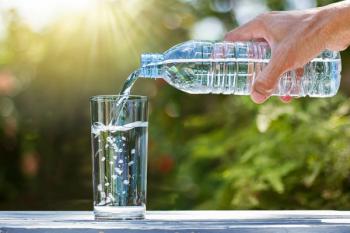 Hand holding drinking water bottle pouring water into glass on wooden table on blurred green nature background | Image Credit: © shark749 - stock.adobe.com