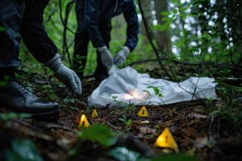 Two forensic investigators in protective gear examine a crime scene in a dense forest, marking evidence near a body covered with a white sheet, surrounded by lush greenery. Generated with AI. | Image Credit: © Milos - stock.adobe.com