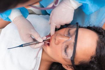 Wide view of dentist applying composite filling to a lower premolar of a female patient wearing protective glasses during treatment. | Image Credit: © Mdv Edwards - stock.adobe.com