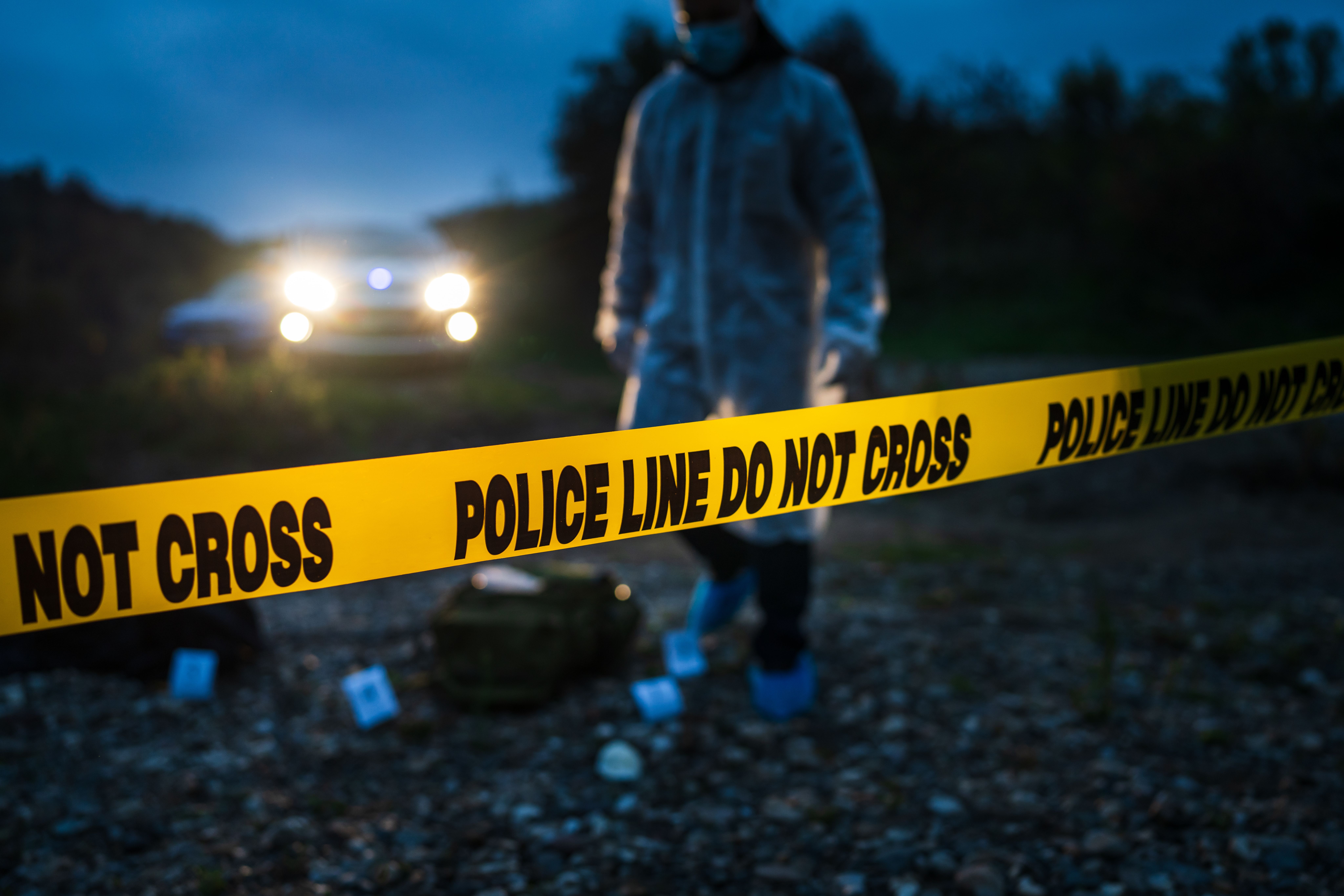 Forensic police investigator collecting evidence at the crime scene by the river in nature at night selective focus on police line tape. | Image Credit: © Miljan Živković - stock.adobe.com