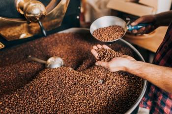 Man's hands holding freshly roasted aromatic coffee beans over a modern coffee roasting machine. | Image Credit: © hedgehog94 - stock.adobe.com