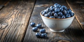 A bowl of fresh blueberries sits on a rustic wooden table, several berries scattered nearby. Generated with AI. | Image Credit: © Collection - stock.adobe.com 