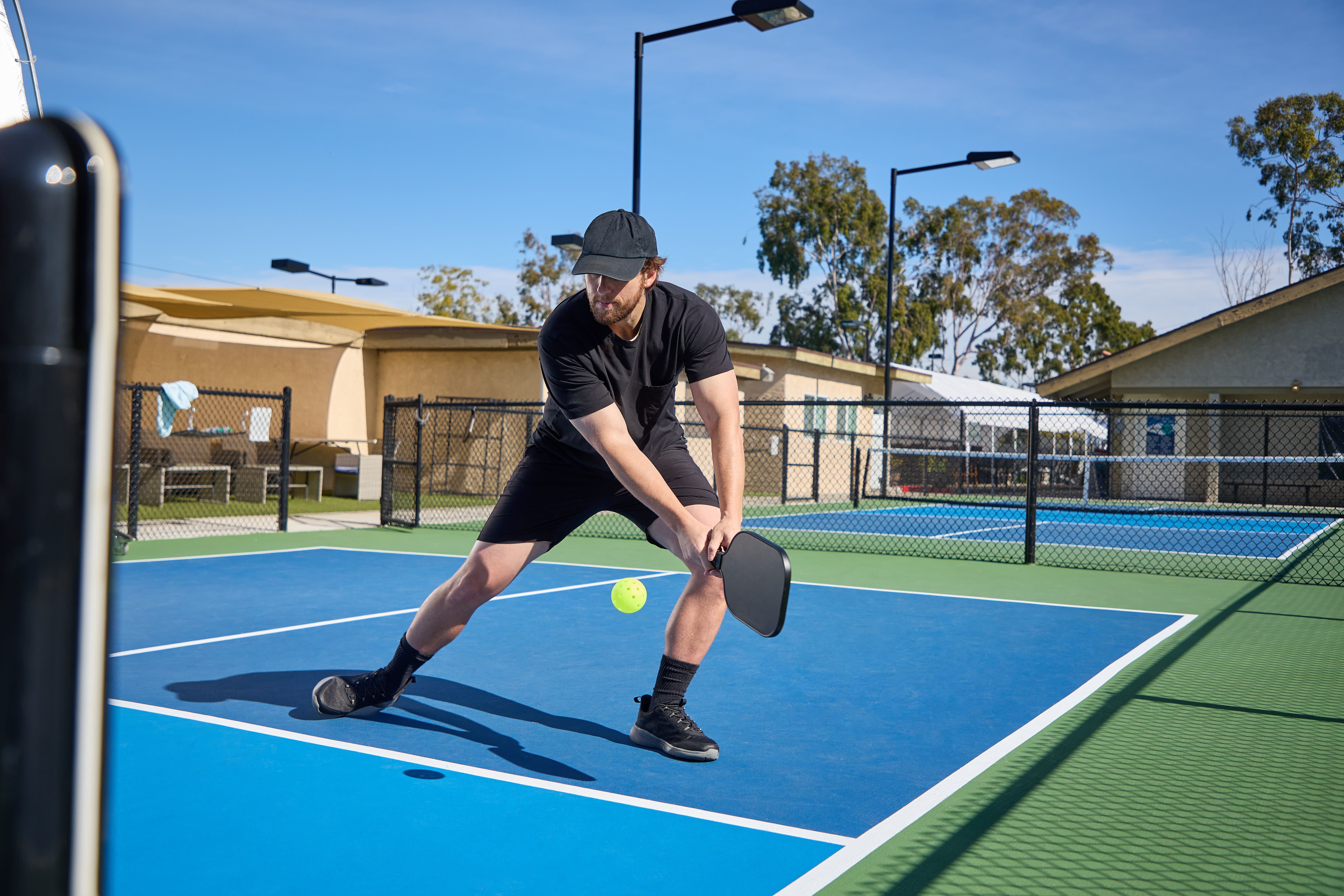 A man dressed in black plays pickleball on a blue court | Image Credit: © joescarnici - stock.adobe.com