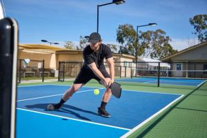 A man dressed in black plays pickleball on a blue court | Image Credit: © joescarnici - stock.adobe.com
