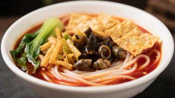 A bowl of River Snail Rice Noodles with a rich red broth, a few green vegetables, and several black mussels on top. Generated with AI. | Image Credit: © Moose - stock.adobe.com