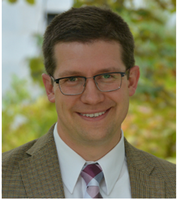 Man with brown hair wearing a plaid suit, white dress shirt, and purple tie.