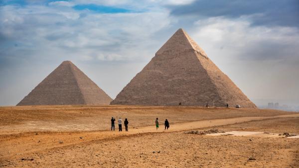 Tourists seen taking photos of the Great Pyramids of Giza from the desert in Egypt - an iconic archaeological and travel destination. | Image Credit: © Mihir Joshi - stock.adobe.com