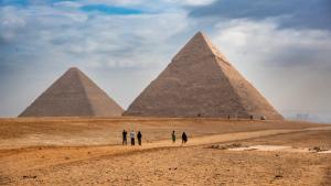 Tourists seen taking photos of the Great Pyramids of Giza from the desert in Egypt - an iconic archaeological and travel destination. | Image Credit: © Mihir Joshi - stock.adobe.com