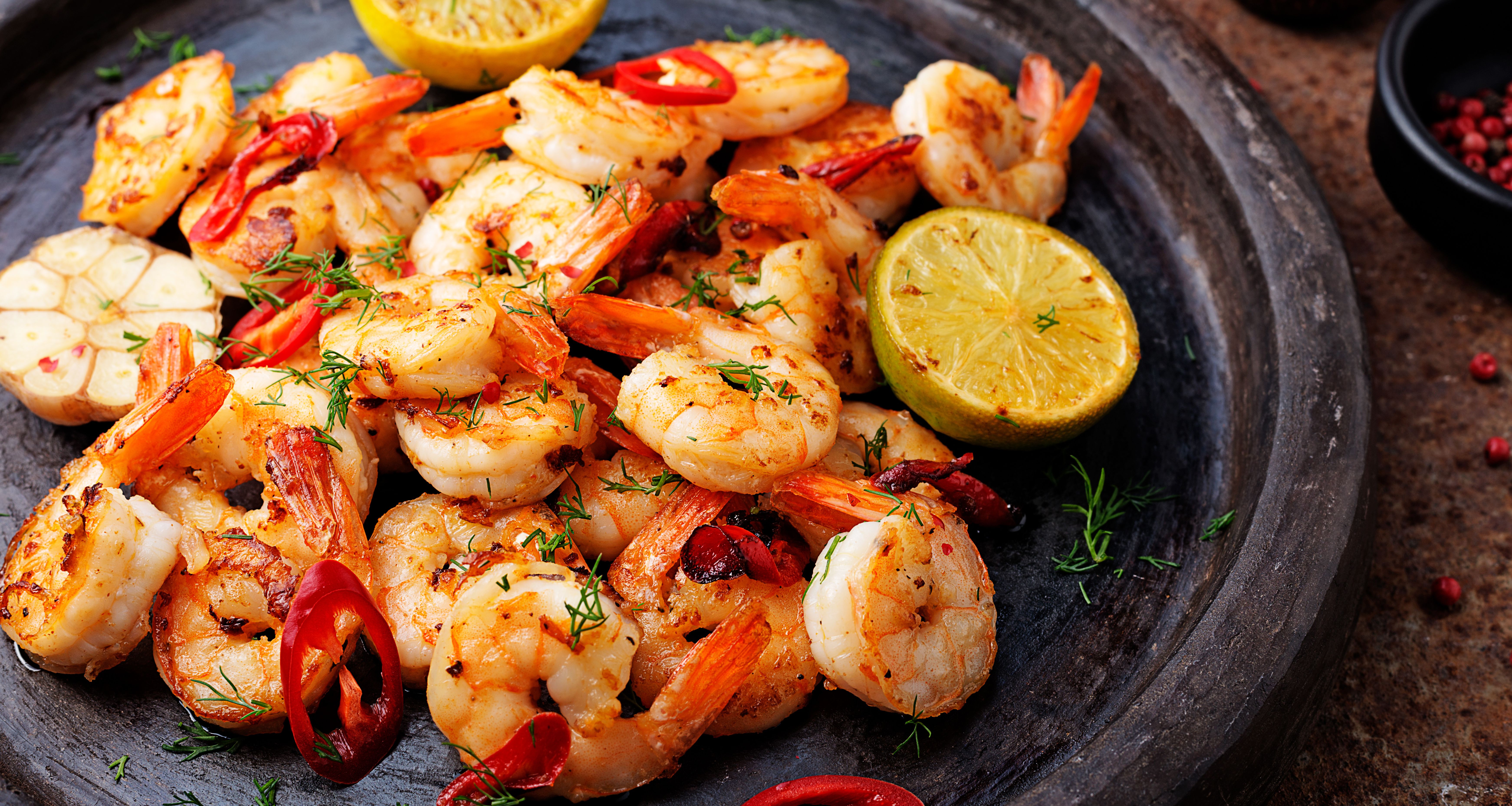 Prawns Shrimps roasted on pan with lemon and garlic on dark rustic background. top view. | Image Credit: © Nelea Reazanteva - stock.adobe.com. 