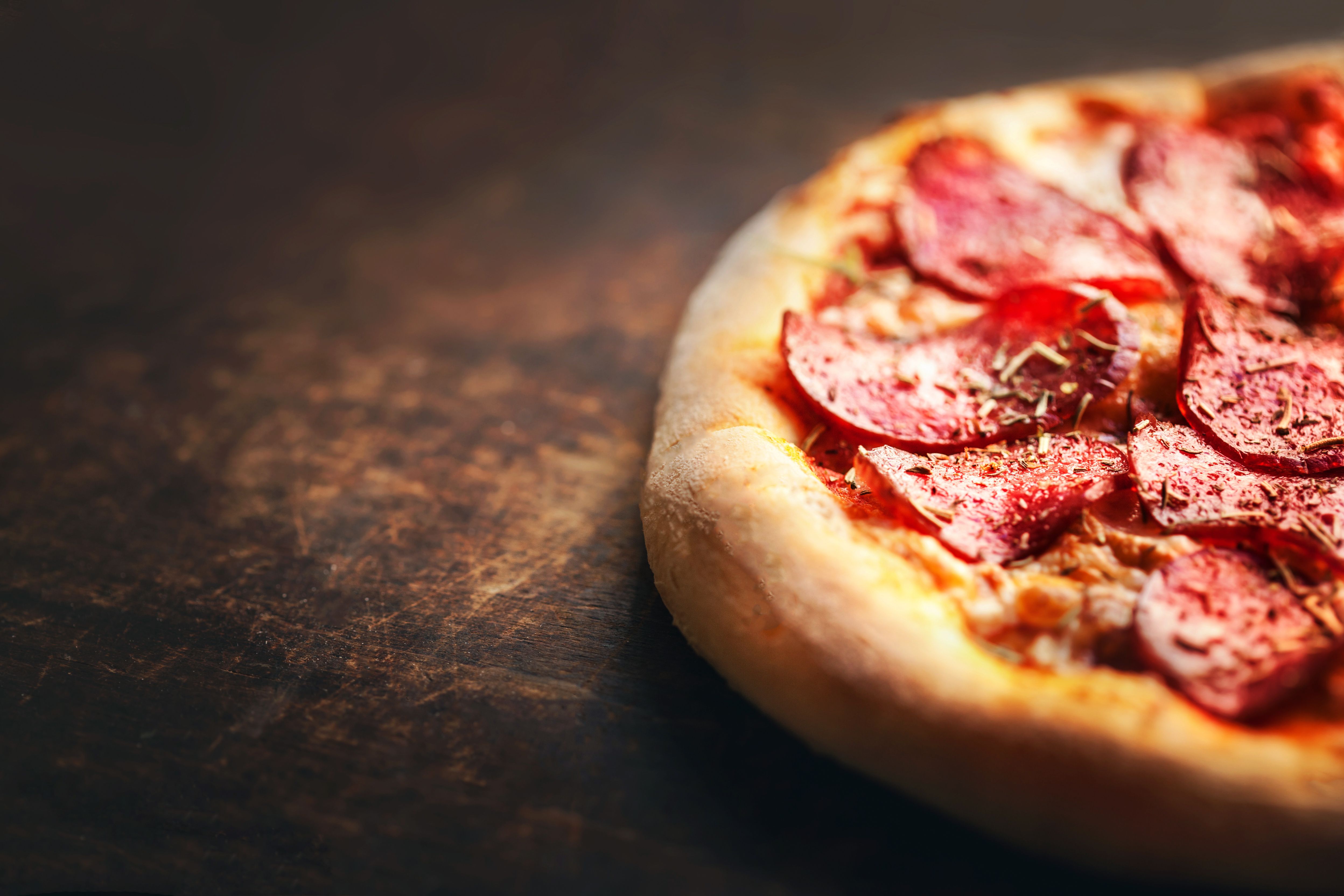 Pizza with pepperoni and salami on a rustic wooden table.