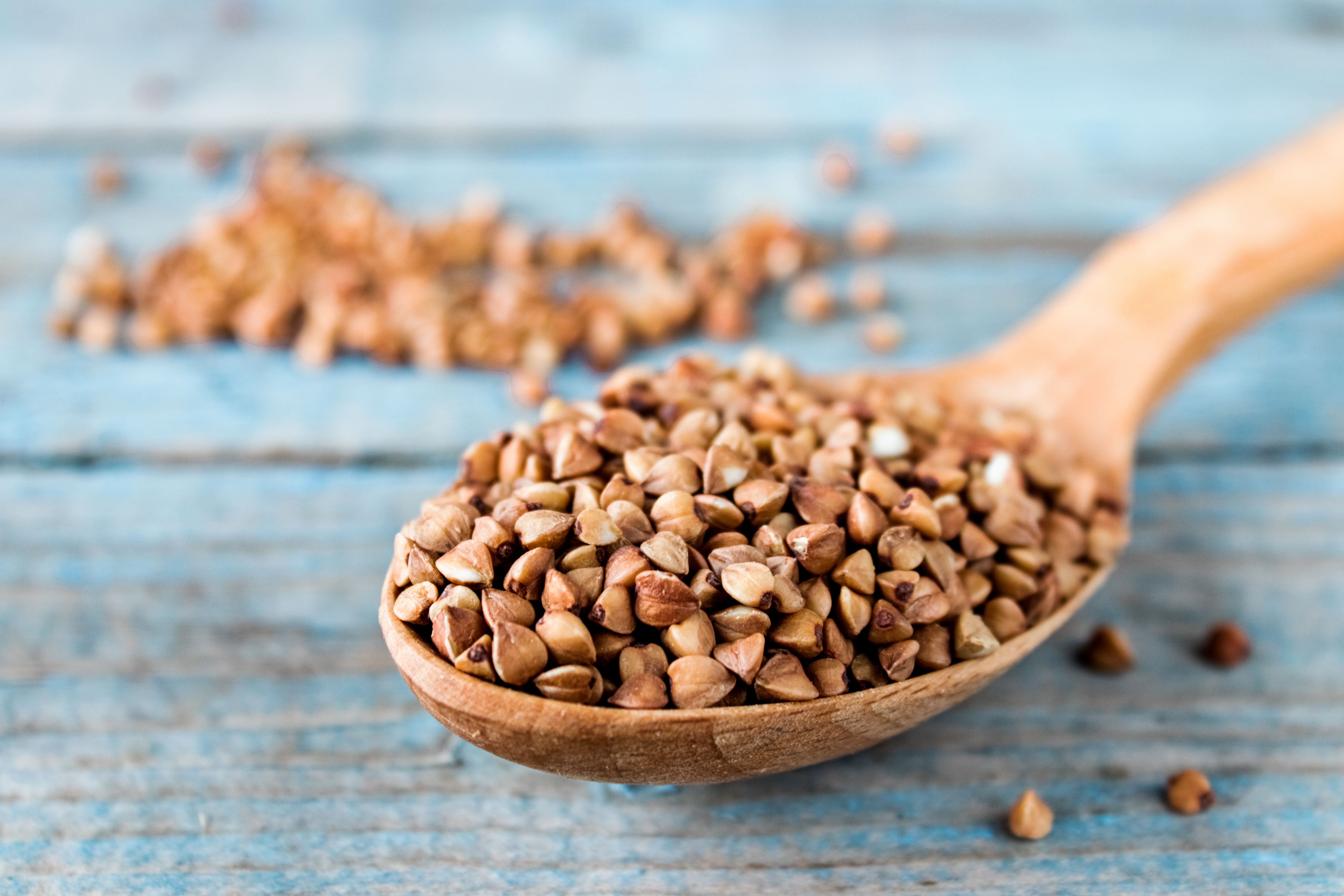Uncooked buckwheat in a spoon on blue old boards. Buckwheat is used for cooking. | Image Credit: © Maryna Osadcha - stock.adobe.com