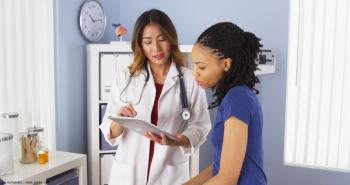 Asian female doctor using a tablet to explain information to an African-American female patient