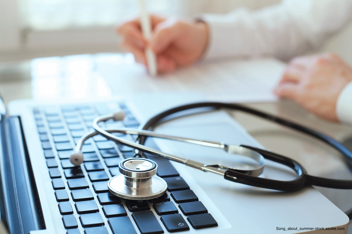 blurred doctor writing in the background, stethoscope lying on laptop