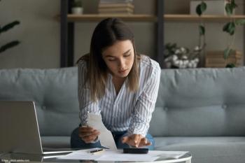 Young woman sitting on couch paying bills
