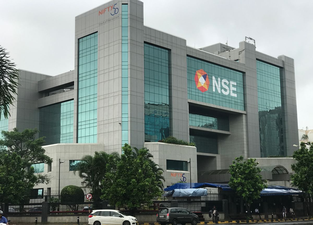 Glass-and-stone exterior of the NSE office building with the NSE logo and Nifty 50 signs, trees and cars in front