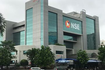 Glass-and-stone exterior of the NSE office building with the NSE logo and Nifty 50 signs, trees and cars in front