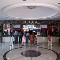 People stand at a cinema box office counter in a marble-floored lobby while a uniformed guard walks past on the right