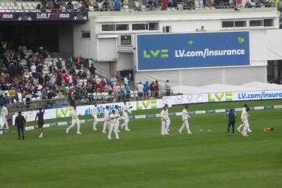 Indian players in white kit walk across the field during a Test match, with spectators in the stands.