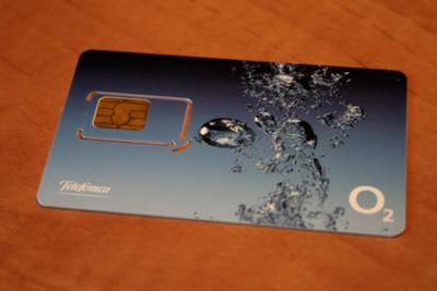 A blue prepaid SIM card with water droplets and a Telefónica O2 logo, lying on a wooden table