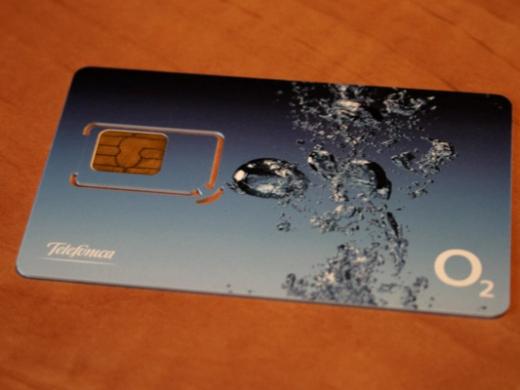 A blue prepaid SIM card with water droplets and a Telefónica O2 logo, lying on a wooden table