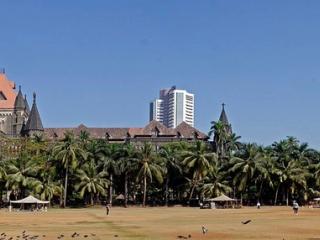 Oval Maidan in Mumbai with the Bombay High Court, a white tower and Rajabai Clock Tower behind palm trees.