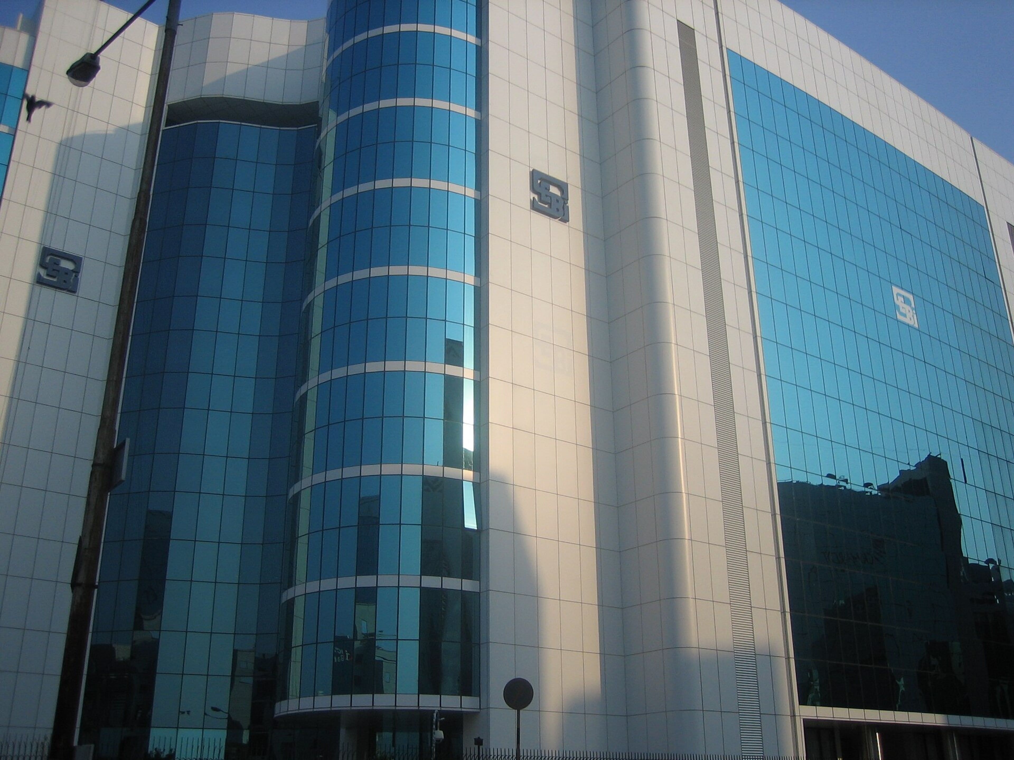 Glass-clad SEBI Bhavan office tower in Mumbai, with blue-tinted windows and the SEBI logo on its facade, in daylight.