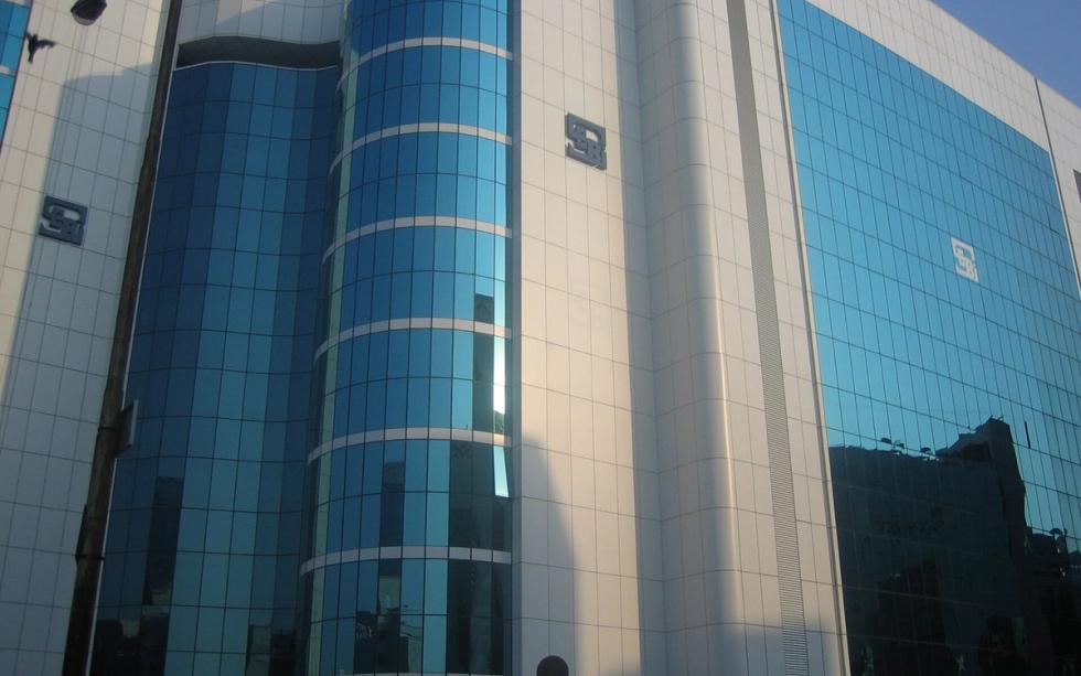 Exterior of a blue-glass office tower with curved bays and SEBI logos, shot in daylight.
