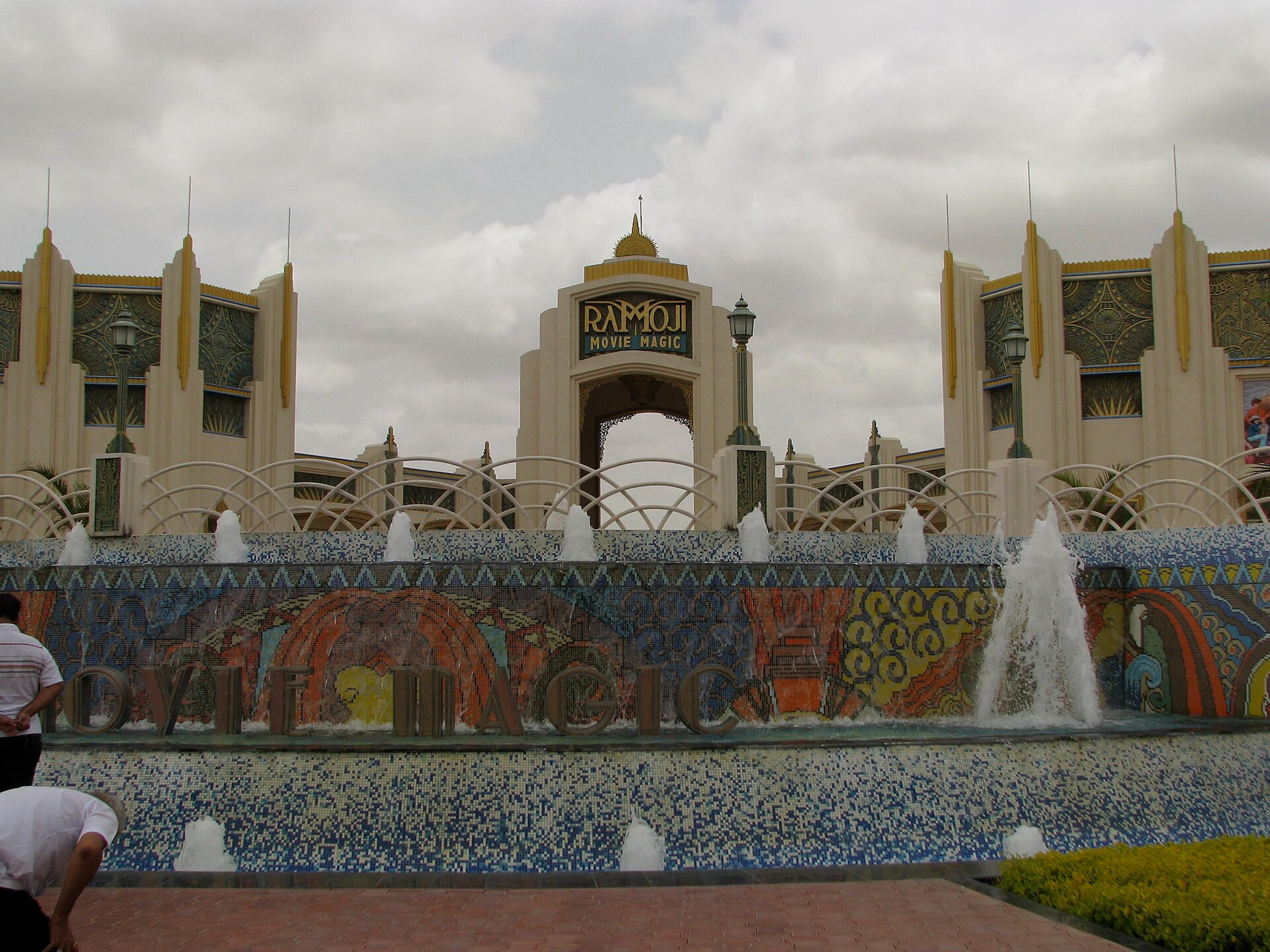 Ornate entrance gate of Ramoji Film City with fountains and mosaic 'Movie Magic' lettering under a cloudy sky.