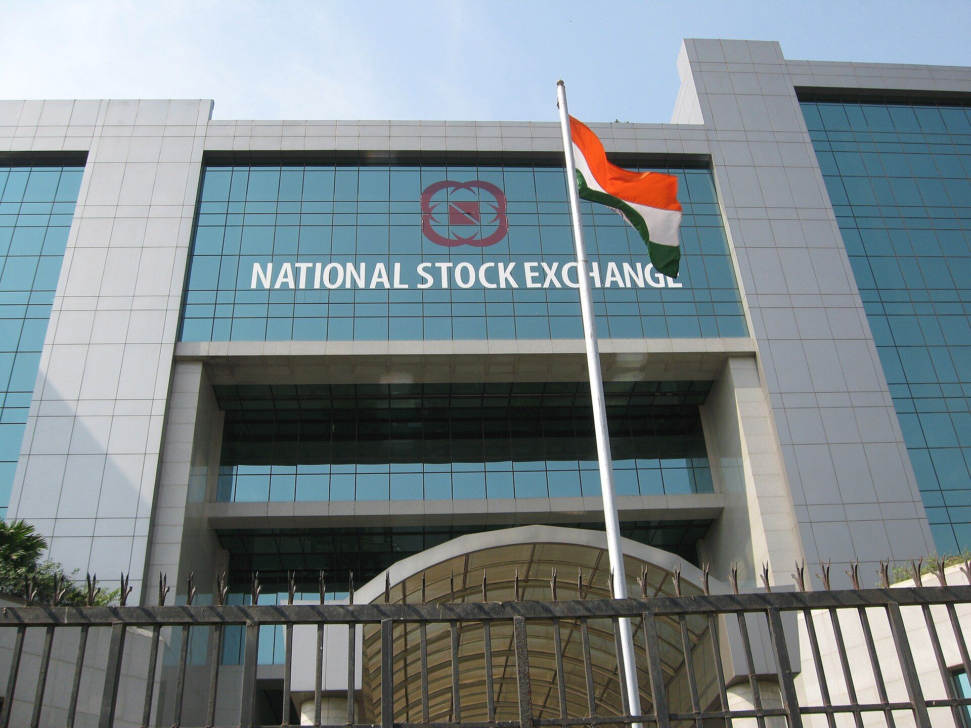 Glass-fronted National Stock Exchange building with its name on the facade and an Indian flag on a pole in front
