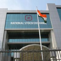 Glass-fronted National Stock Exchange building with its name on the facade and an Indian flag on a pole in front